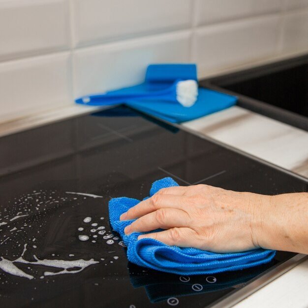 mao-de-uma-mulher-com-um-pano-de-microfibra-azul-esfrega-uma-placa-de-ceramica-de-vidro-na-cozinha_111599-906
